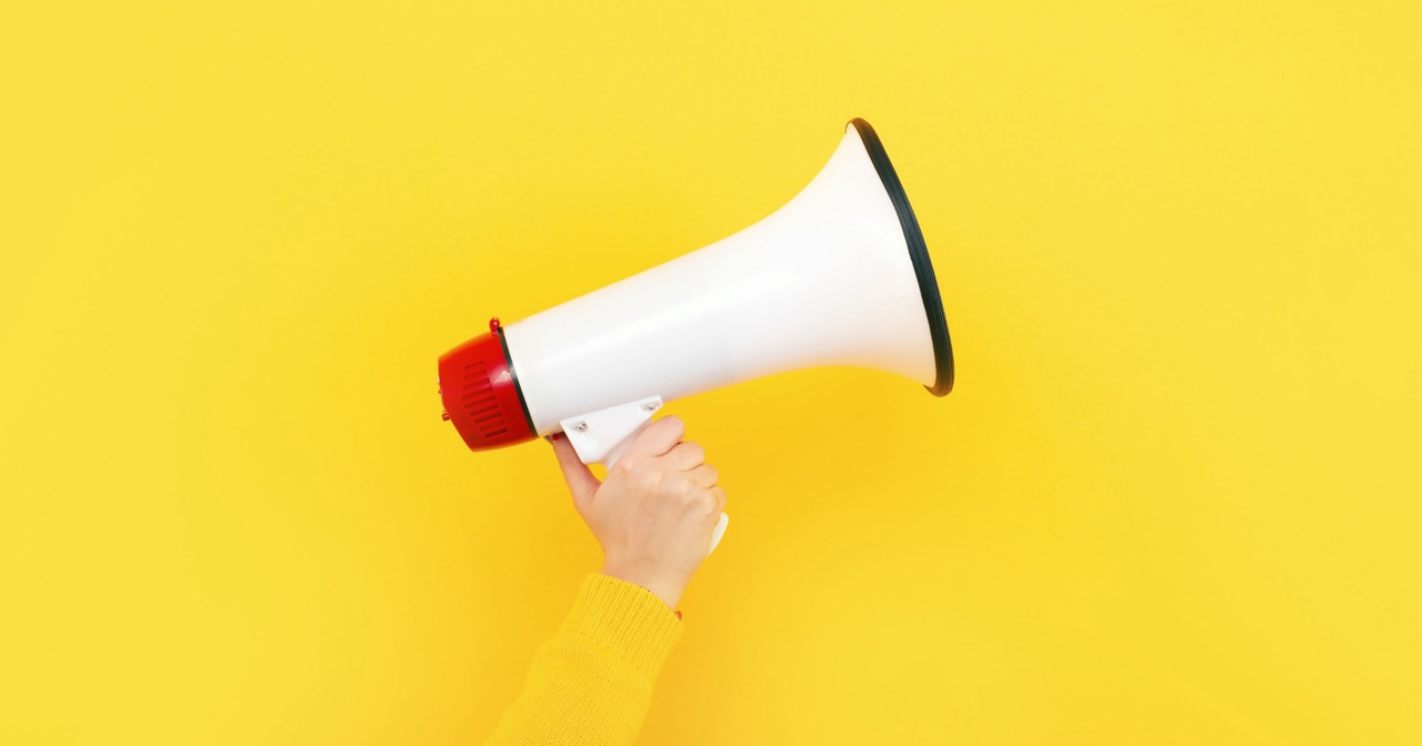 Hot Takes In Marketing For 2026 A hand holding a white marketing megaphone with a red end stands out against a bright yellow background.