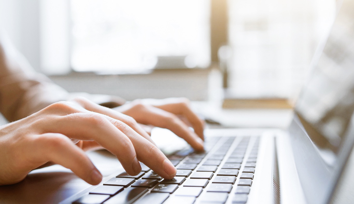 Your Website Might Be The Reason Your Marketing Isn’t Working Close-up of a person's hands typing on a laptop keyboard, sunlight streaming in through a window, as they work on nonprofit projects.